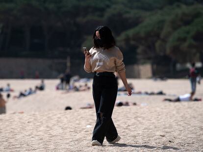 Una mujer pasea mientras consulta su teléfono móvil por la playa de Castell-Platja D'Aro, cerca de Girona, este miércoles.