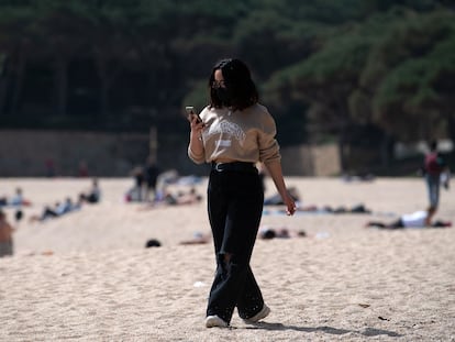 Una mujer pasea mientras consulta su teléfono móvil por la playa de Castell-Platja D'Aro, cerca de Girona, este miércoles.