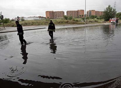 Dos bomberos observan la inundación en la rotonda de Fuente Carrantona, en Moratalaz. Abajo, atasco junto al Arco del Triunfo. 
/ R. GUTIÉRREZ