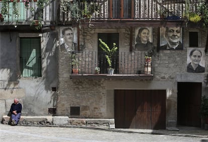 Un vecino sentado bajo una fachada con los retratos de una de las familias de Mogarraz.