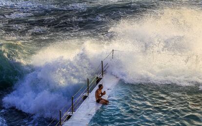 Un hombre se sienta en el borde de una piscina en el Club de Natación Bondi Icebergs mientras las olas rompen a su lado, en Sidney (Australia).