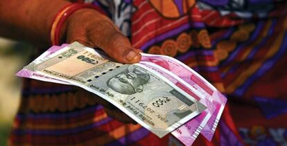 Una mujer sostiene tres billetes de rupias indias. 