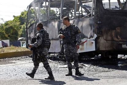 Polícia estatal ao lado de um ônibus de passageiros carbonizado, cujas chamas foram apagadas pelos bombeiros de Guadalajara, México.