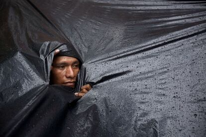 Indígena Mbyá Guaraní olha através de buraco no plástico que o protege da chuva que cai sobre o acampamento montado em frente ao Indi (Instituto Paraguaio do Indígena, na tradução).