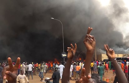 With the headquarters of the ruling party burning in the back, supporters of mutinous soldiers demonstrate in Niamey, Niger, Thursday, July 27 2023