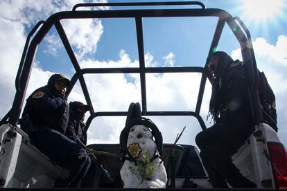 Tres elementos de la policía posan junto a un muñeco de nieve que construyeron sobre su camioneta de patrulleo.