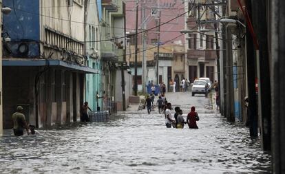 Varias personas caminan dentro del agua en una calle inundada de la capital cubana.