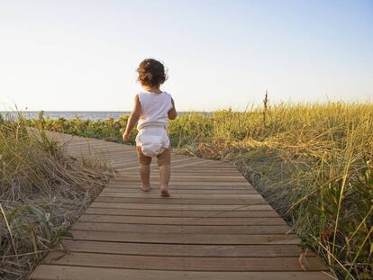 Una niña camnian por la playa con su pañal. 