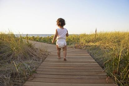 Una niña camnian por la playa con su pañal. 