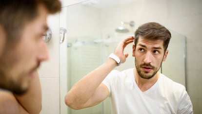 El reflejo del cristal de un hombre tocándose el pelo en el baño.