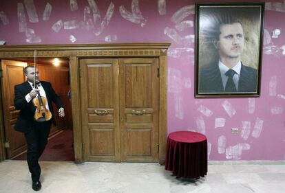 Un miembro de la Orquesta Nacional Siria porta su instrumento mientras pasa ante un retrato del presidente Bachar El Assad, antes de un concierto benéfico en Damasco, el pasado 21 de noviembre.