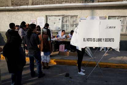 Una mujer prepara su voto mientras otras personas esperan para emitir sus votos para gobernador del Estado de México en una mesa de votación en Nezahualcoyotl.