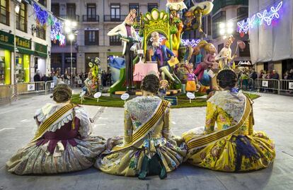 Tres falleras descansan frente a una falla instalada en la plaza de la Merced.