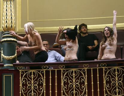 Las tres activistas de Femen se ponen en pie en sus asientos en la tribuna de invitados. A la derecha, Lara Alcázar, líder del movimiento en España.