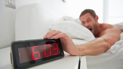 Un hombre apagando el despertador por la mañana.