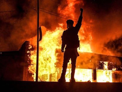 Manifestante ergue o braço em frente a um edifício em chamas incendiado durante protesto em Minneápolis.