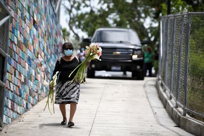 Una mujer acompaña la precesión del entierro, cargando flores frente a uno de los coches fúnebres que transporta los restos de los migrantes.