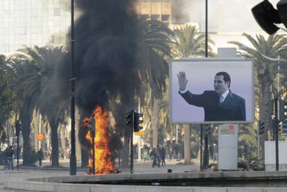 El humo de un incendio causado por unos manifestantes se ve detrás de un cartel con la imagen del presidente tunecino.