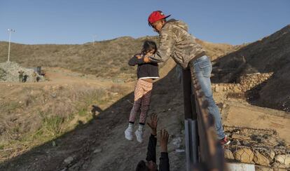 Un migrante atraviesa con una niña la frontera en San Diego (California).