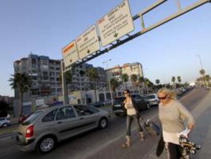 Dos turistas pasan junto a la cola de coches que espera para entrar al peñón, hoy en la Línea de la Concepción (Cádiz). EFE/Archivo