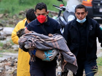 Un paramédico de seguridad pública lleva a un niño luego de que un deslizamiento de tierra de una colina aplastara una casa debido al paso del huracán 'Grace', en el barrio Loma Bonita en Xalapa.