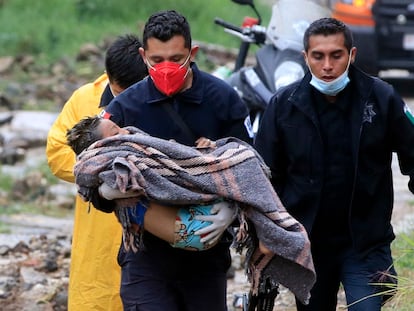 Un paramédico de seguridad pública lleva a un niño luego de que un deslizamiento de tierra de una colina aplastara una casa debido al paso del huracán 'Grace', en el barrio Loma Bonita en Xalapa.