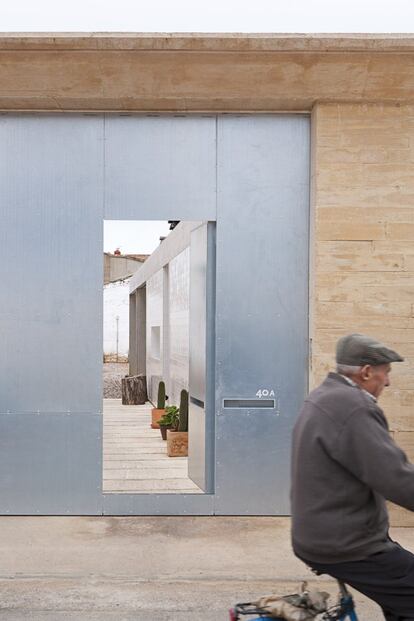 Una puerta de acero continúa el muro de adobe y gana intimidad para el patio por el que se accede a la vivienda.