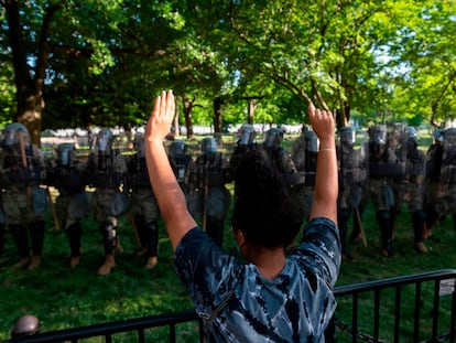A protestor raises her hands near a line of National Guard soldiers deployed near the White House on June 1, 2020 as demonstrations against George Floyd's death continue. - Police fired tear gas outside the White House late Sunday as anti-racism protestors again took to the streets to voice fury at police brutality, and major US cities were put under curfew to suppress rioting.With the Trump administration branding instigators of six nights of rioting as domestic terrorists, there were more confrontations between protestors and police and fresh outbreaks of looting. Local US leaders appealed to citizens to give constructive outlet to their rage over the death of an unarmed black man in Minneapolis, while night-time curfews were imposed in cities including Washington, Los Angeles and Houston. (Photo by ROBERTO SCHMIDT / AFP) / ALTERNATE CROP