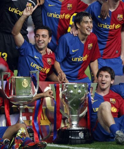 Xavi, Bojan e Messi posam com a Copa do Rei e a taça da Liga no Camp Nou após saírem vencedores das duas competições em 2009.