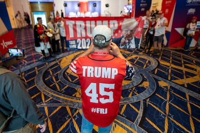 A la CPAC, que se celebra hasta el sábado en el Gaylord National Resort & Convention Center en National Harbor, han asistido miles de seguidores del expresidente Donald Trump para mostrar su apoyo camino a las elecciones del próximo año. En la imagen, un hombre con una camiseta con el nombre de Trump estampado  en el reverso fotografía un cartel en apoyo al exmandatario.