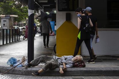 Una mujer mira a un hombre sin hogar que duerme en el suelo en la calle comercial Hamra, en Beirut, Líbano.