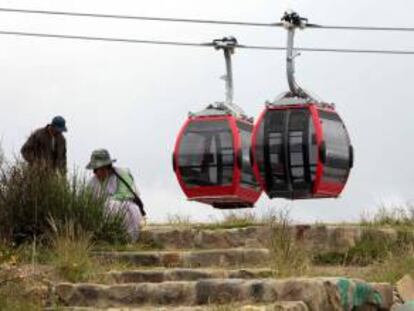 Una mujer permanece sentada mientras el teleférico que la empresa austríaca Doppelmayr pasa detrás en El Alto (Bolivia). EFE/Archivo