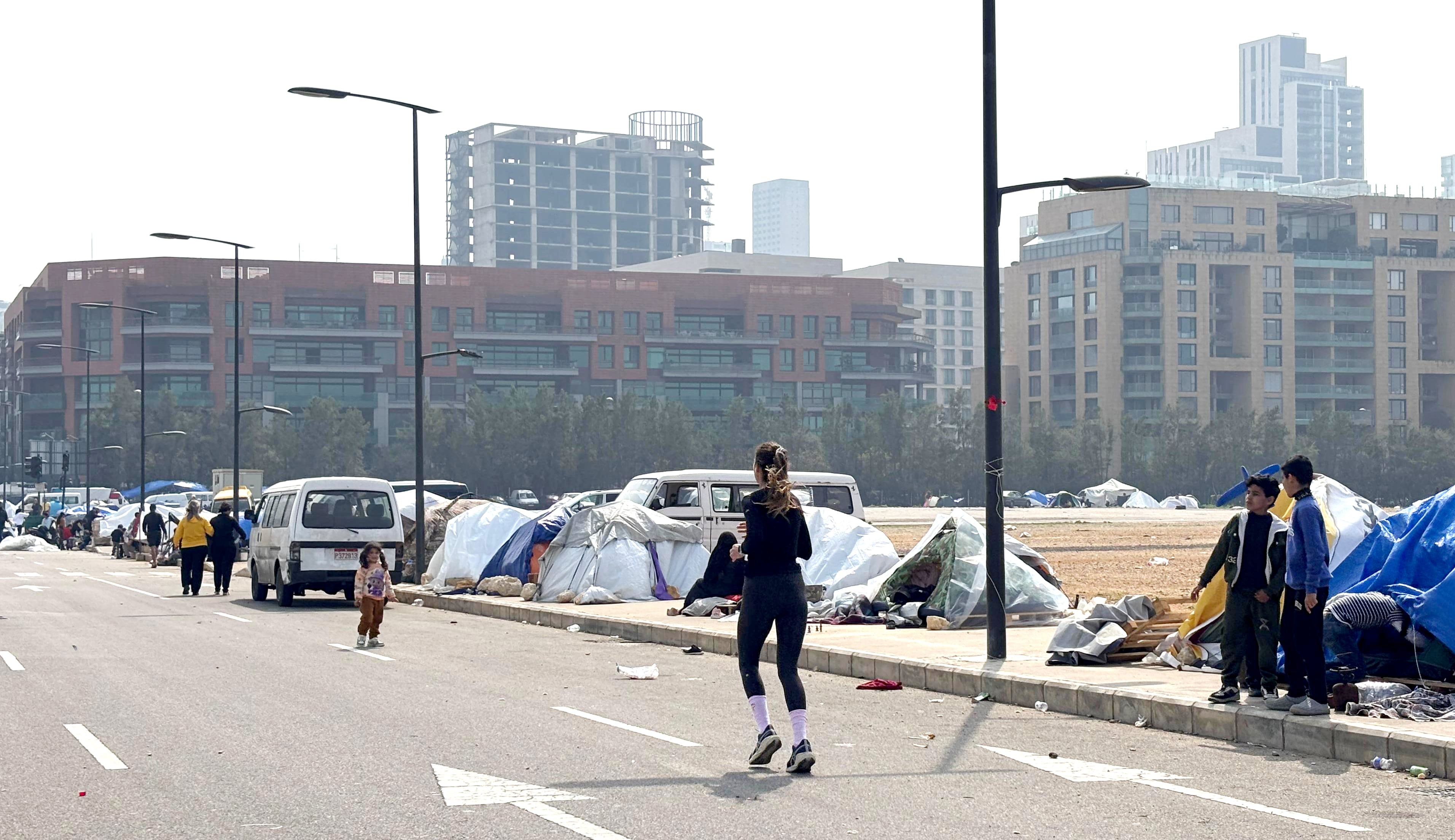 Una mujer hace deporte ante las tiendas de campaña donde se abarrotan familias desplazadas en el frente marítimo de Beirut.
