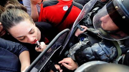 Una mujer se pinta los labios frente al escudo de un policía junto al edificio del gobierno macedonio en Skopje (Macedonia).