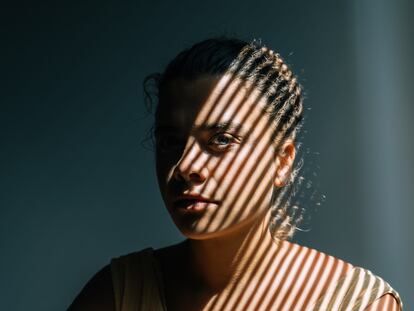 Portrait of mid adult woman with blinds shadows on woman. The theme of depression, abuse and mental problems.