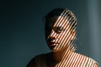 Portrait of mid adult woman with blinds shadows on woman. The theme of depression, abuse and mental problems.