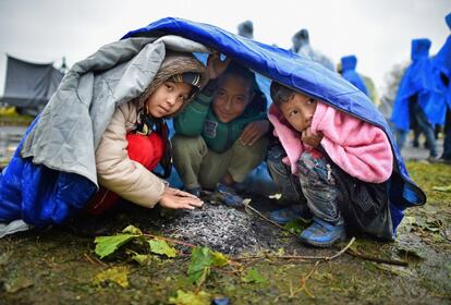 Un grupo de niños refugiados esperan bajo la lluvia en la frontera entre Croacia y Eslovenia en Trnovec (Croacia). Las tensiones entre Croacia y Eslovenia han aumentado desde que Hungría cerrara sus fronteras y Liubliana decidiera limitar el número diario de aspirantes a asilo que permite entrar en el país.