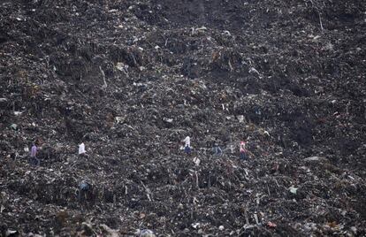 Varias personas caminan por un vertedero mientras continúan las labores de rescate después de un derrumbamiento cerca de una zona en Gazipur, en Nueva Delhi (India).