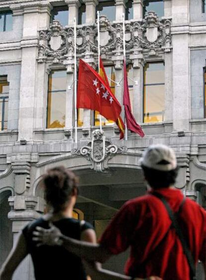 Dos transeúntes observan las banderas a media asta en el palacio de Cibeles.