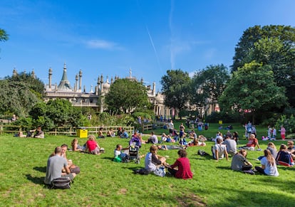 Jóvenes sentados en el césped frente al Royal Pavilion, Brighton, en Inglaterra, Reino Unido.