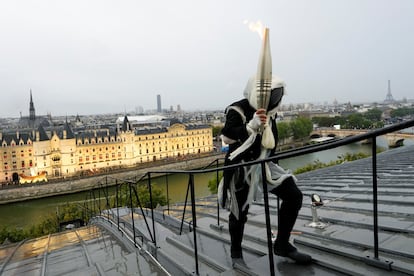 Un personaje porta la antorcha olímpica sobre los tejados de París.