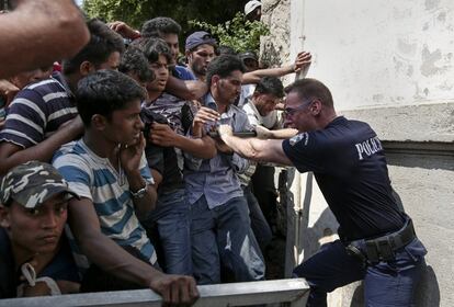 Un policía griego trata de controlar a los inmigrantes que esperan un procedimiento de registro en una comisaría de la isla de Kos.