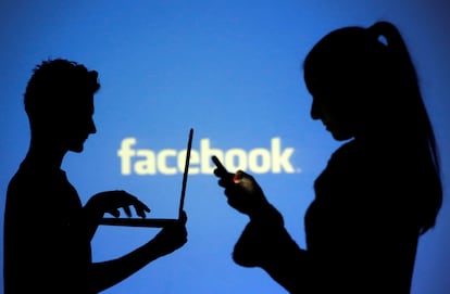 Dos personas, una con un ordenador y otra con un móvil, frente a una pantalla con el logo de Facebook.