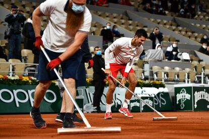 El tenista Novak Djokovic (derecha) ayuda a quitar el agua de la superficie de la pista durante el partido de la tercera ronda de individuales contra el colombiano Daniel Elahi Galan, en Roland Garros, el 3 de octubre. Dos jugadoras inscritas en el cuadro júnior de la competición dieron positivo por coronavirus, por lo que fueron descalificadas en aplicación del protocolo sanitario para luchar contra esa pandemia, indicó este domingo la Federación Francesa de Tenis (FFT).