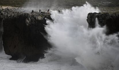 Un grupo de personas en los bufones de Pría (Asturias) caminan por las rocas en una jornada de fuertes vientos que provocó la borrasca Amelie dejando rachas de hasta 130 kilómetros por hora, en la imagen, una ola golpea la costa este lunes.