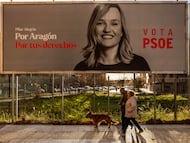 Un hombre y una mujer pasan con un perro por delante de un cartel electoral de Pilar Alegría, candidata a la presidencia de Aragón por el PSOE, en Zaragoza, este lunes.