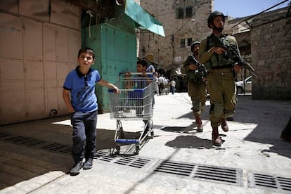 Varios niños palestinos caminan junto a soldados israelíes durante la festividad del 'Pésaj' en la ciudad de Hebrón (Palestina).