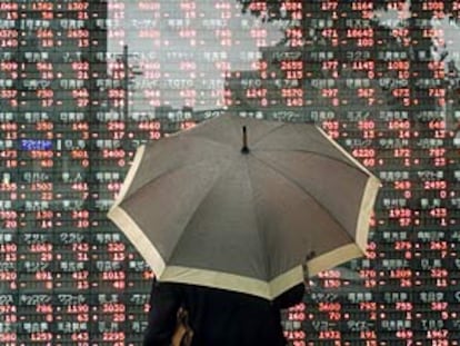 Un transeúnte contempla bajo la lluvia un panel de cotizaciones en las calles de Tokio.