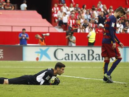 Sergio Rico retiene el bal&oacute;n en el suelo junto al defensa del Barcelona Gerard Piqu&eacute;.