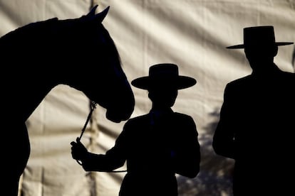 Dos jinetes dialogan mientras sujetan por la rienda a un caballo.